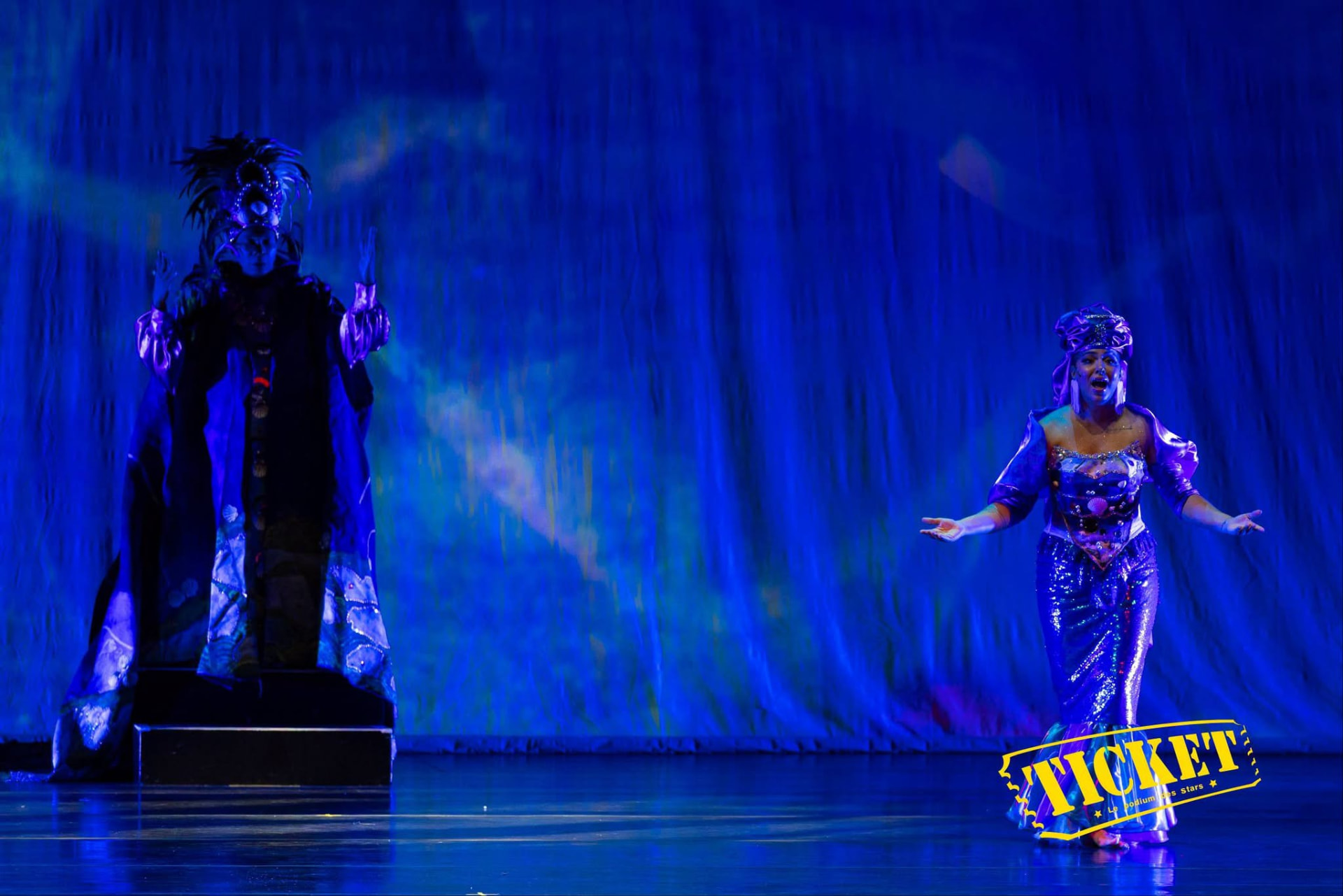 A masked figure and a performer in shimmering blue costume