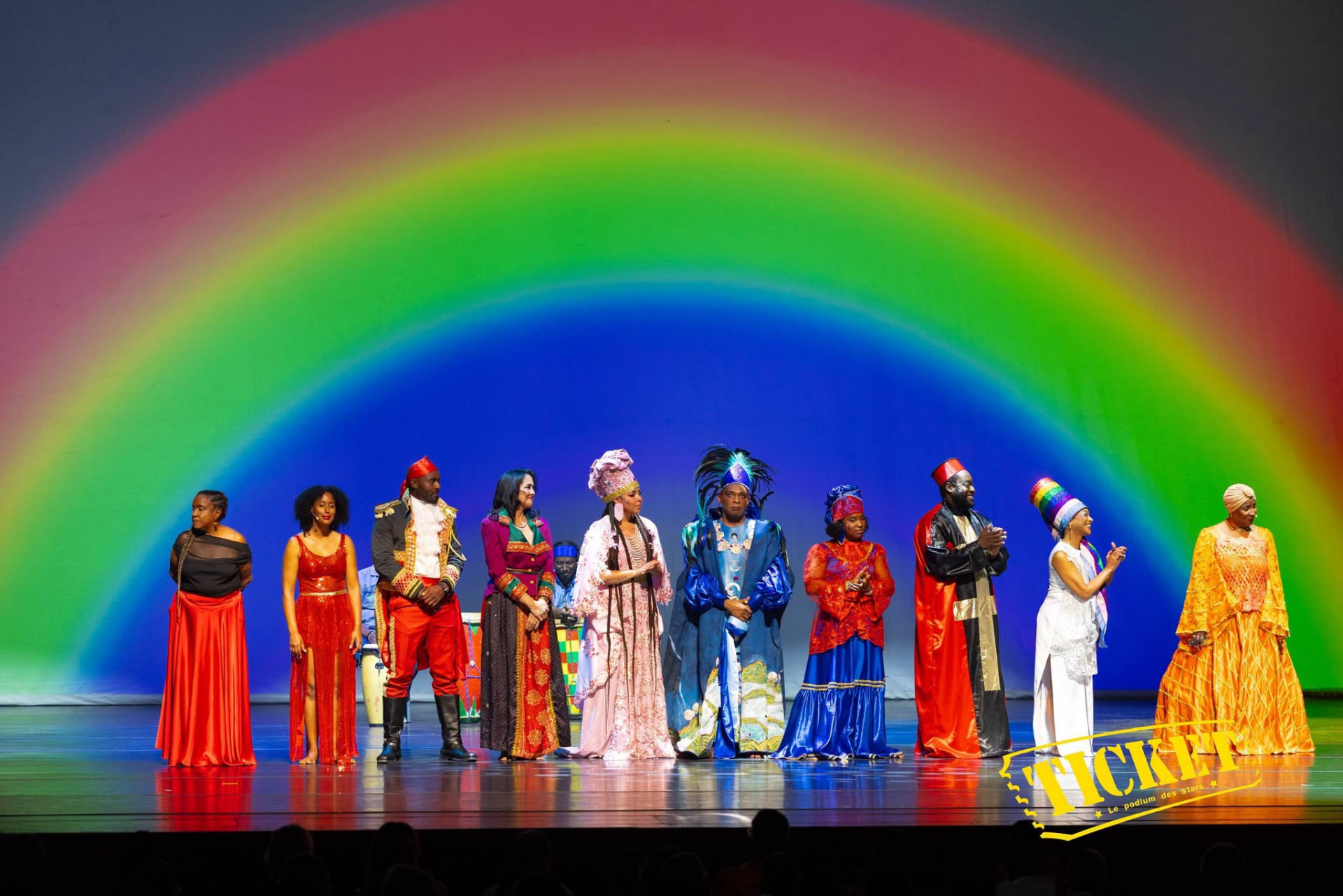 The cast taking a bow before a giant projected rainbow