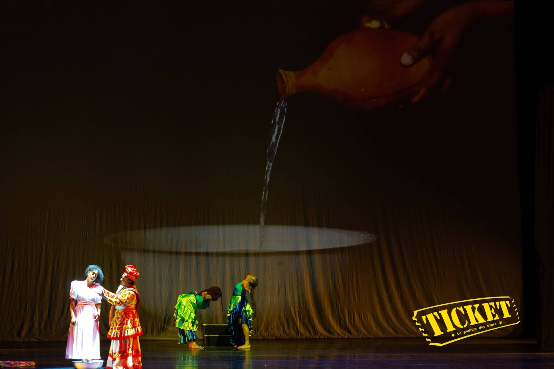 Performers on stage beneath a projected jar pouring water