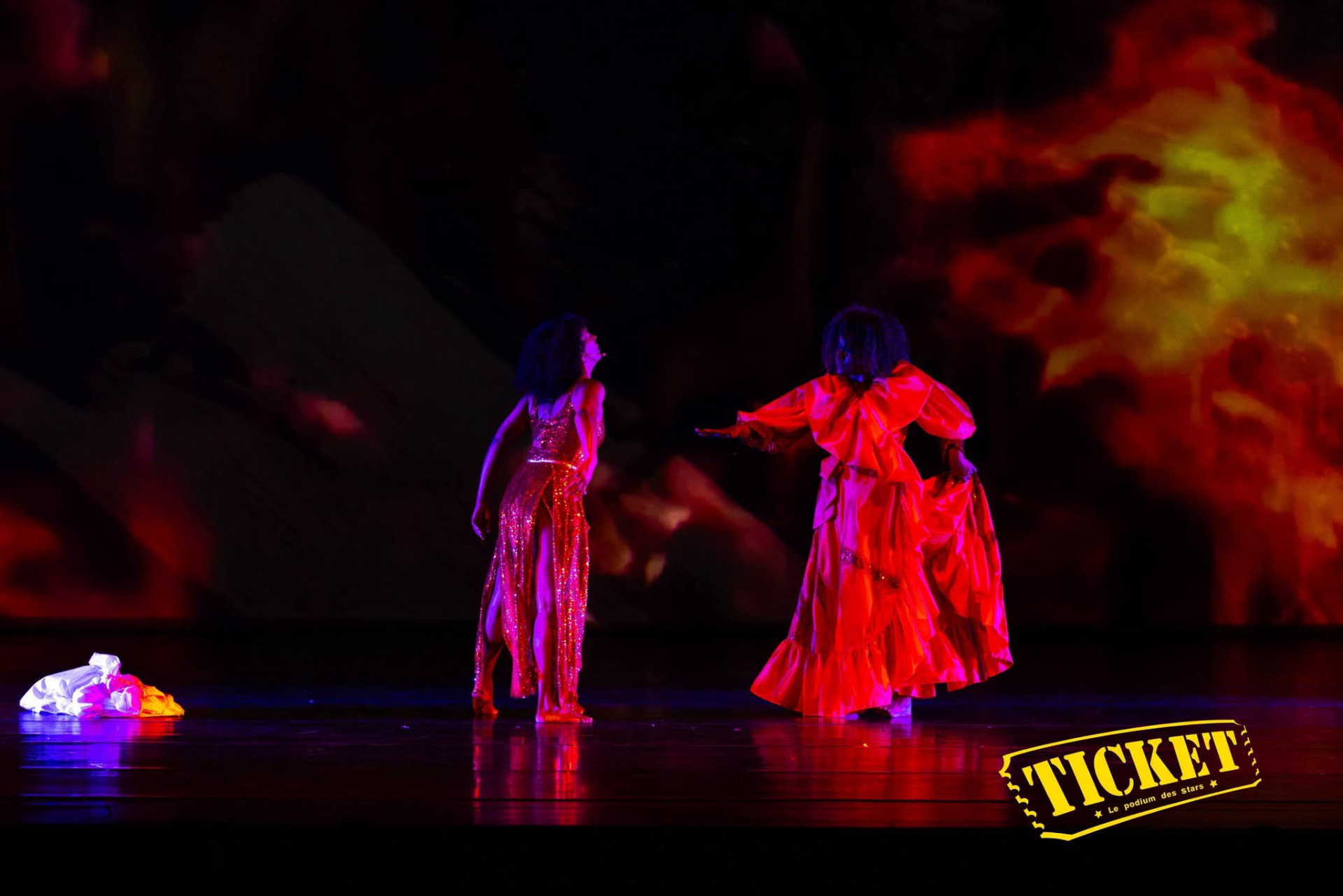 Two dancers in red before a wall of projected flames