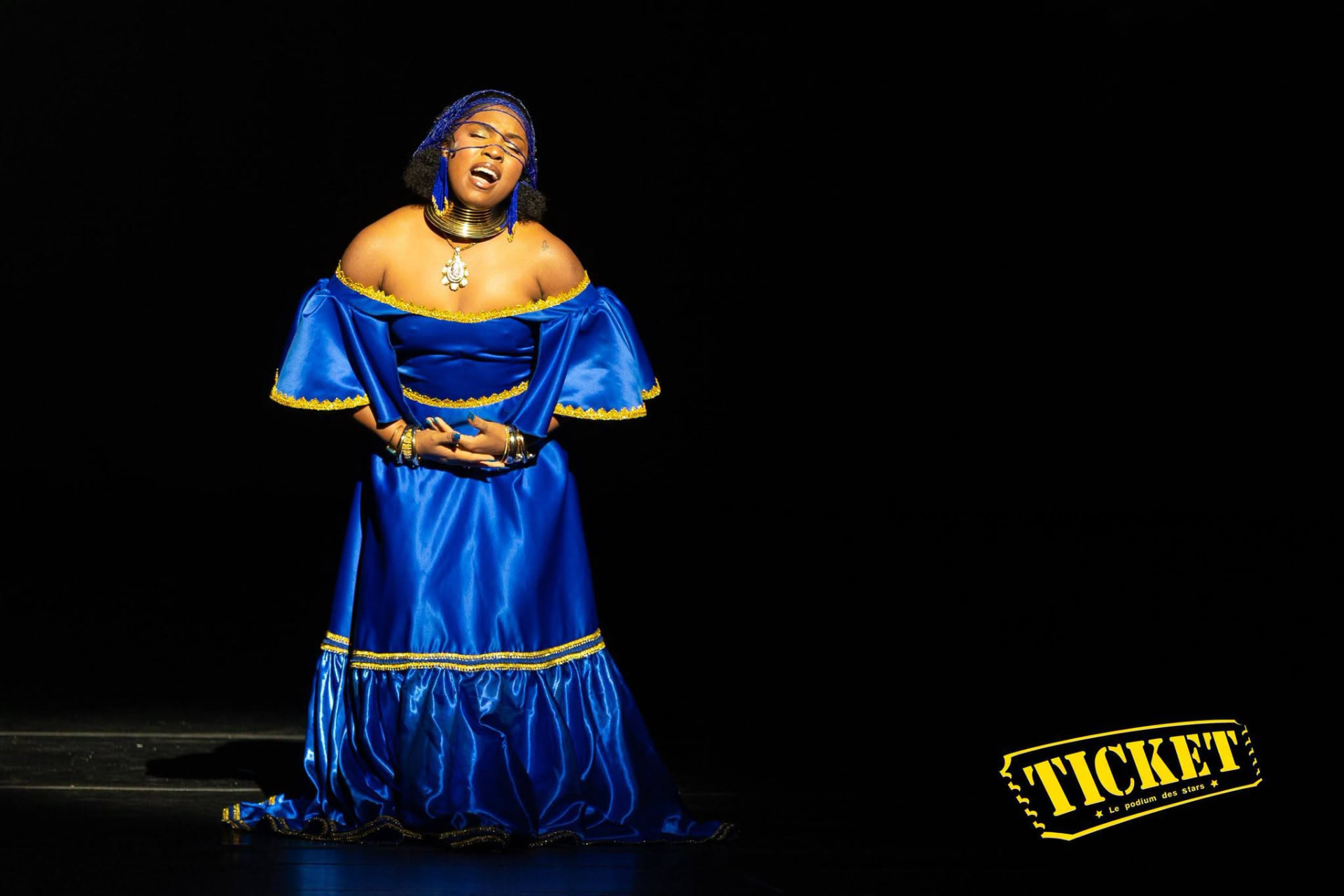 A singer in a blue and gold satin gown mid-song