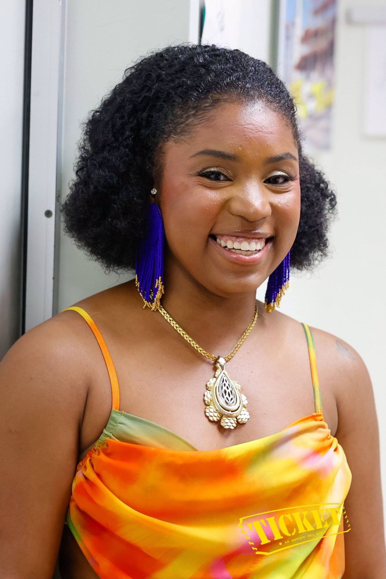 A performer smiling backstage in a bright orange gown