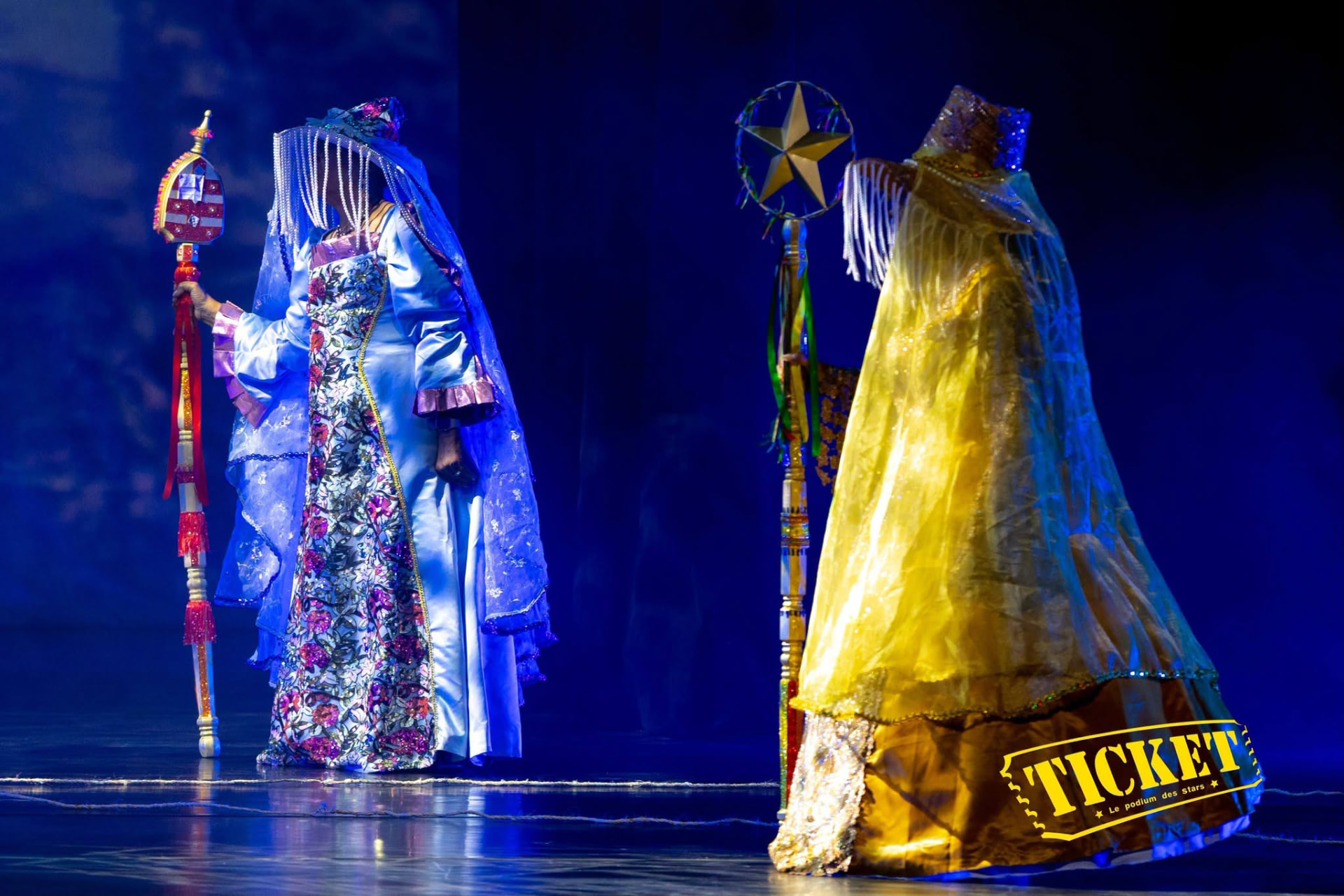 Two performers in blue and gold ceremonial gowns holding staffs