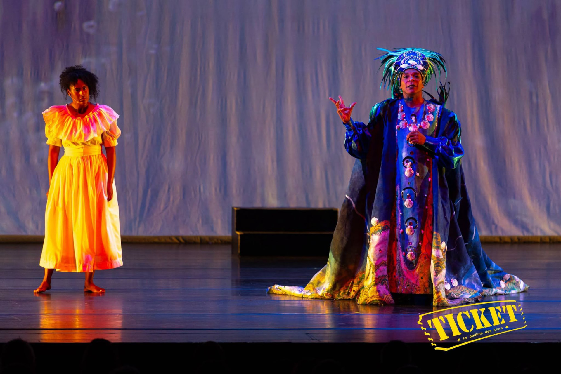 Two performers in yellow and blue costumes in dialogue on stage