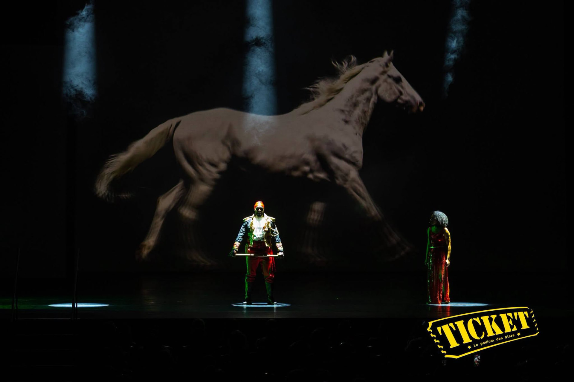 A performer beneath a giant projected horse galloping across the stage