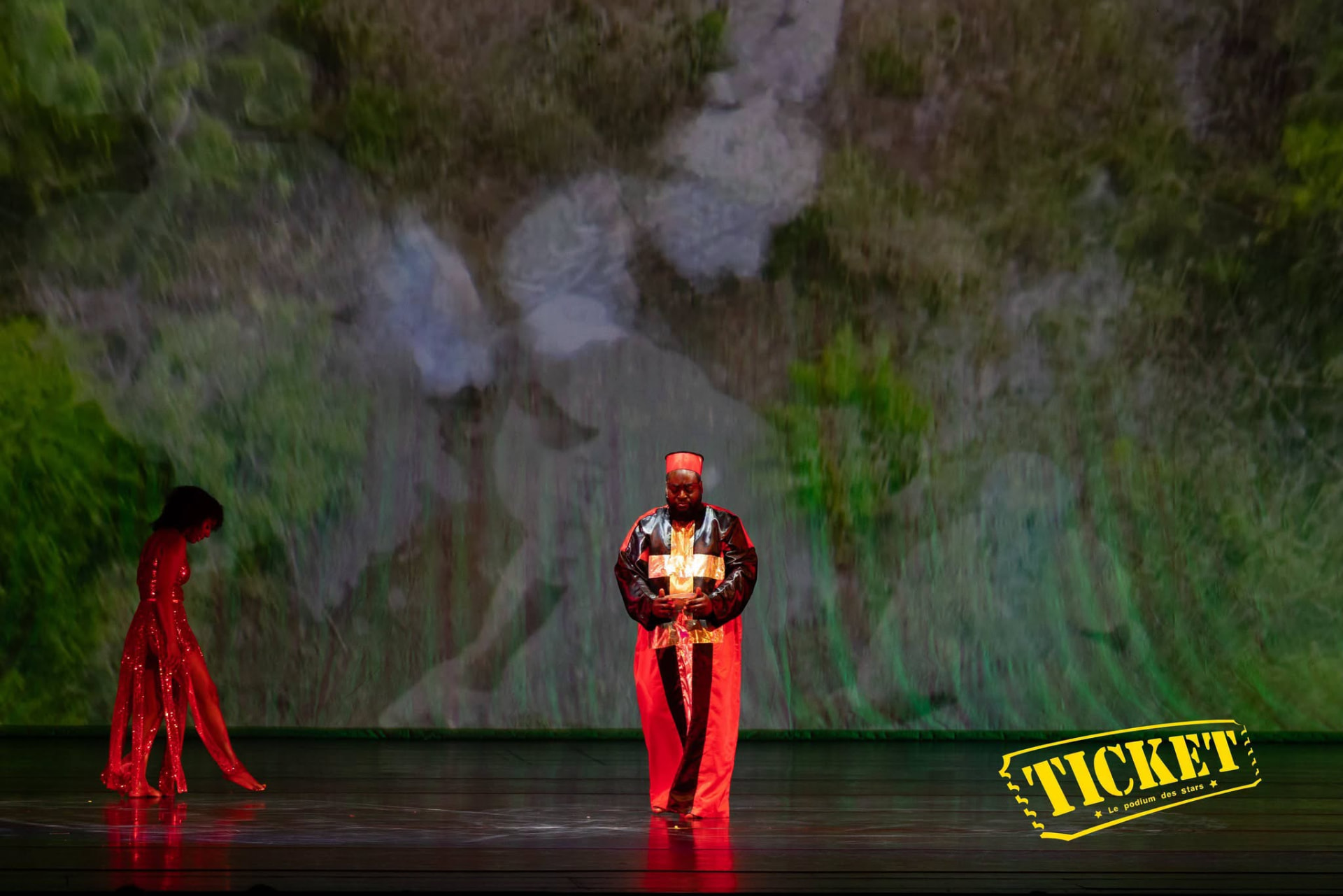 A performer holding a lit offering with a dancer in red