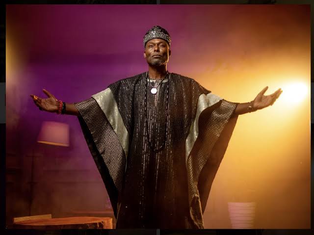 Jimmy performing in a shimmering robe with arms outstretched under warm stage light